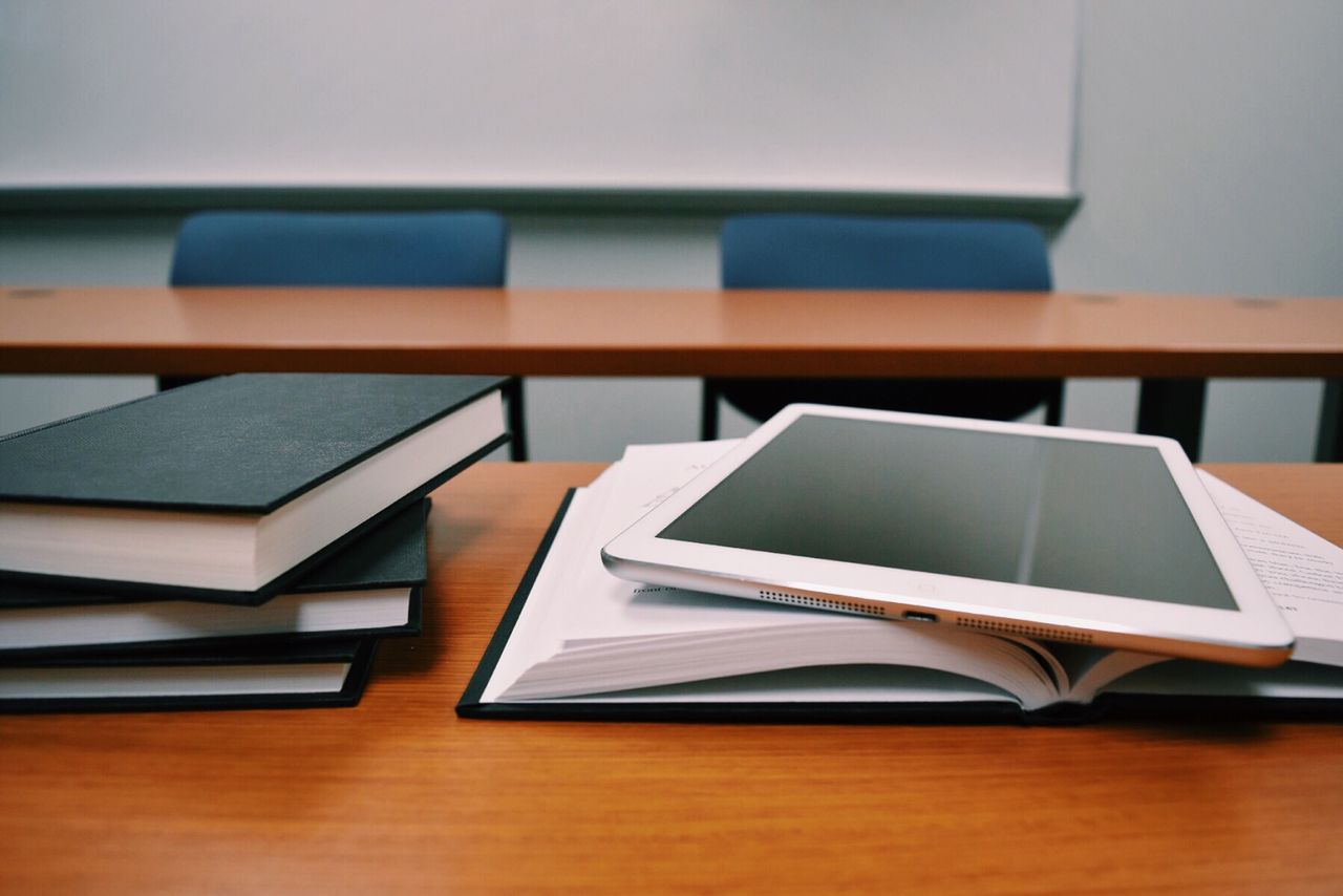 About Books and a tablet on a desk in a classroom, depicting modern education.